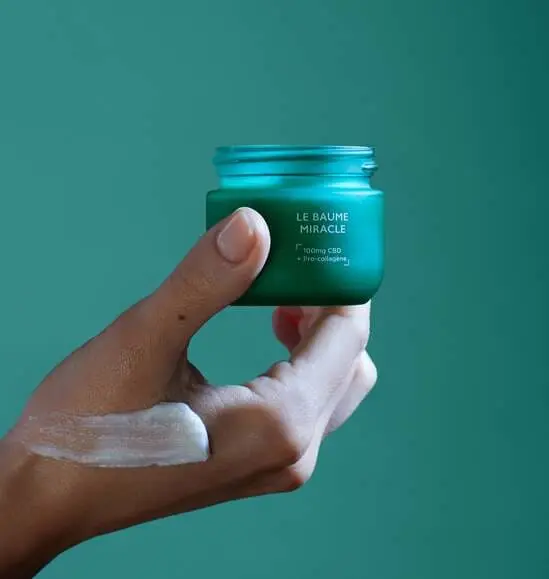 Pot de baume au CBN tenu à la main, texture étalée sur la peau